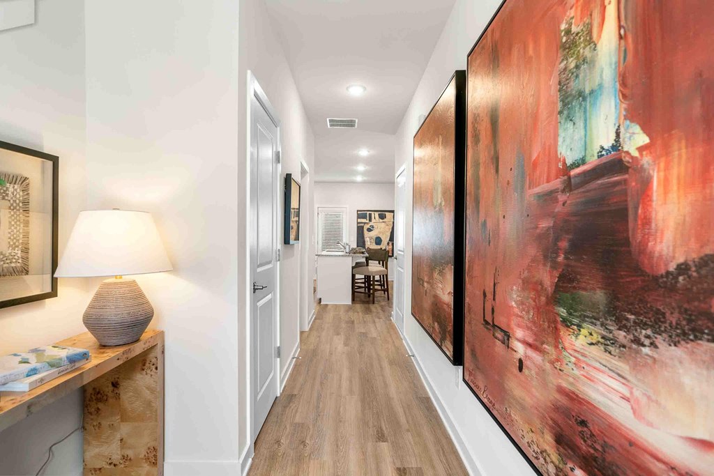 A hallway with a large painting on the wall and a lamp on a table.