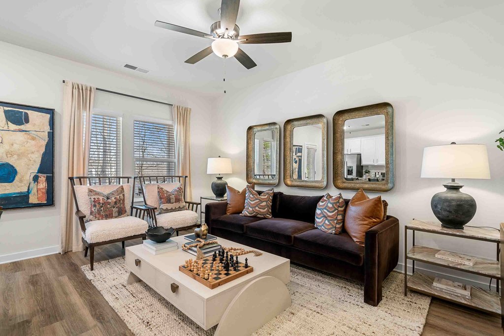 A living room with a brown couch, a chess board, and a ceiling fan.