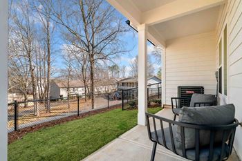 A chair is on a porch with a view of a fence and houses.