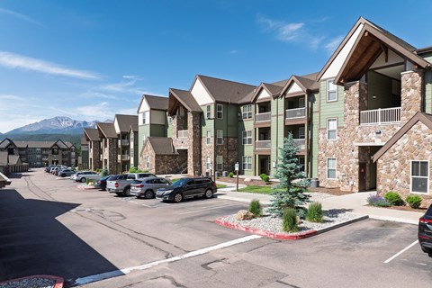 A row of apartment buildings with cars parked in front.