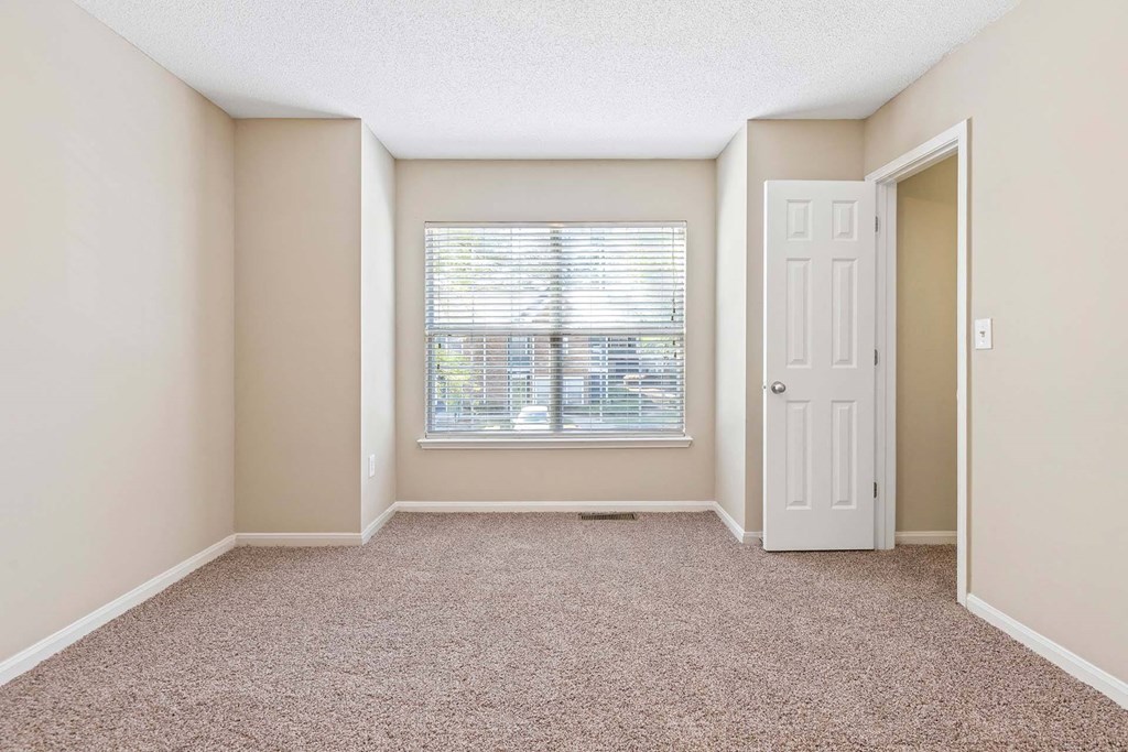 A room with a carpeted floor and a window with blinds.