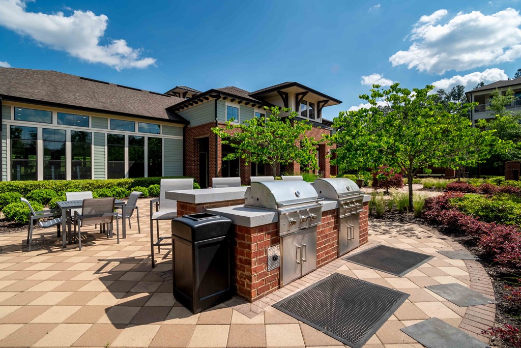 One BR Apartments in Greenville SC - Velo Verdae - Outdoor Grill Station with Brick and Stainless Steel Grill Sets, Counter with Bar Chairs, Table Seating, and Surrounding Trees