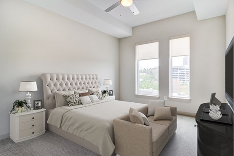 Furnished Apartments in Atlanta, GA - Venue Brookwood - Bedroom with Nightstands, Lamps, Couch, Dresser, TV, Ceiling Fan, and Tall Windows.
