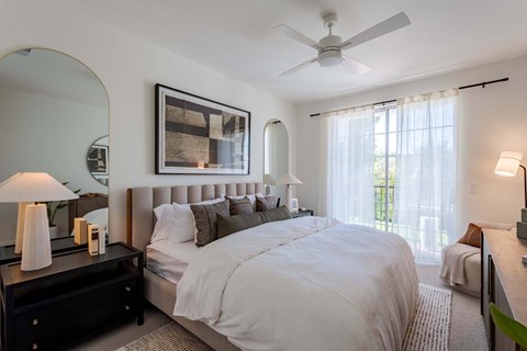 A bedroom with a large bed, a ceiling fan, and a painting on the wall.