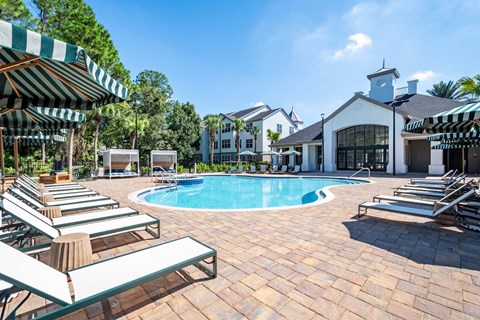 A pool surrounded by lounge chairs and umbrellas with a building in the background.