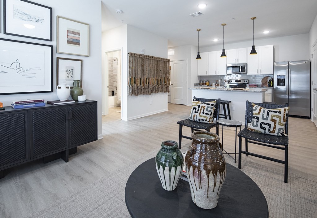 a living room with a table and chairs and a kitchen with a refrigerator