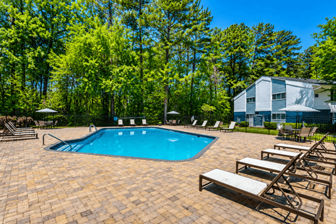 A pool surrounded by trees and chairs.