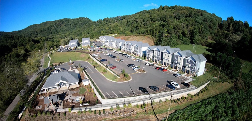 A bird's eye view of a parking lot surrounded by a forest and a building complex.