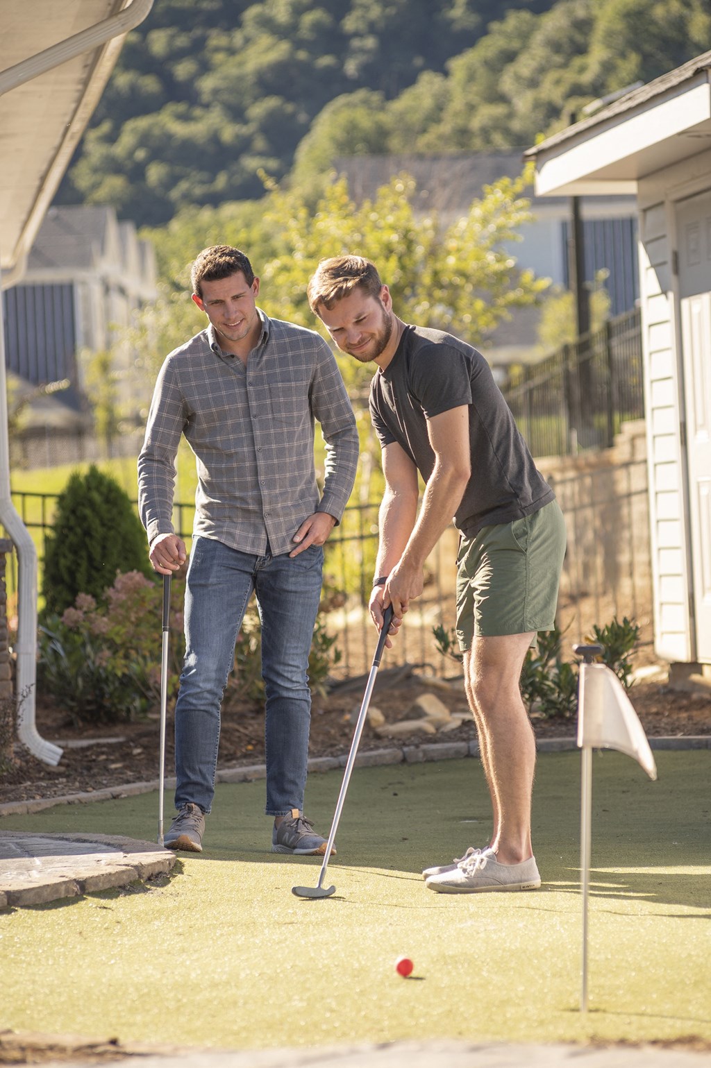 Two men playing mini golf on a sunny day.