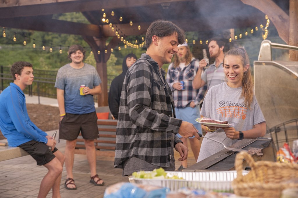 A group of people are gathered around a picnic table under a canopy with string lights.