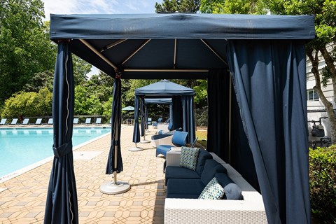 A poolside canopy with blue umbrellas and a couch.