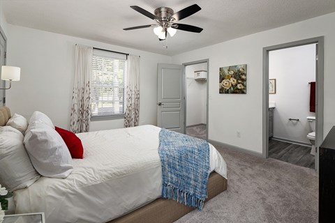 A bedroom with a bed, a ceiling fan, and a door leading to another room.