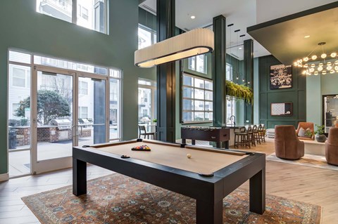 A pool table is in the middle of a room with a green wall and a large window.