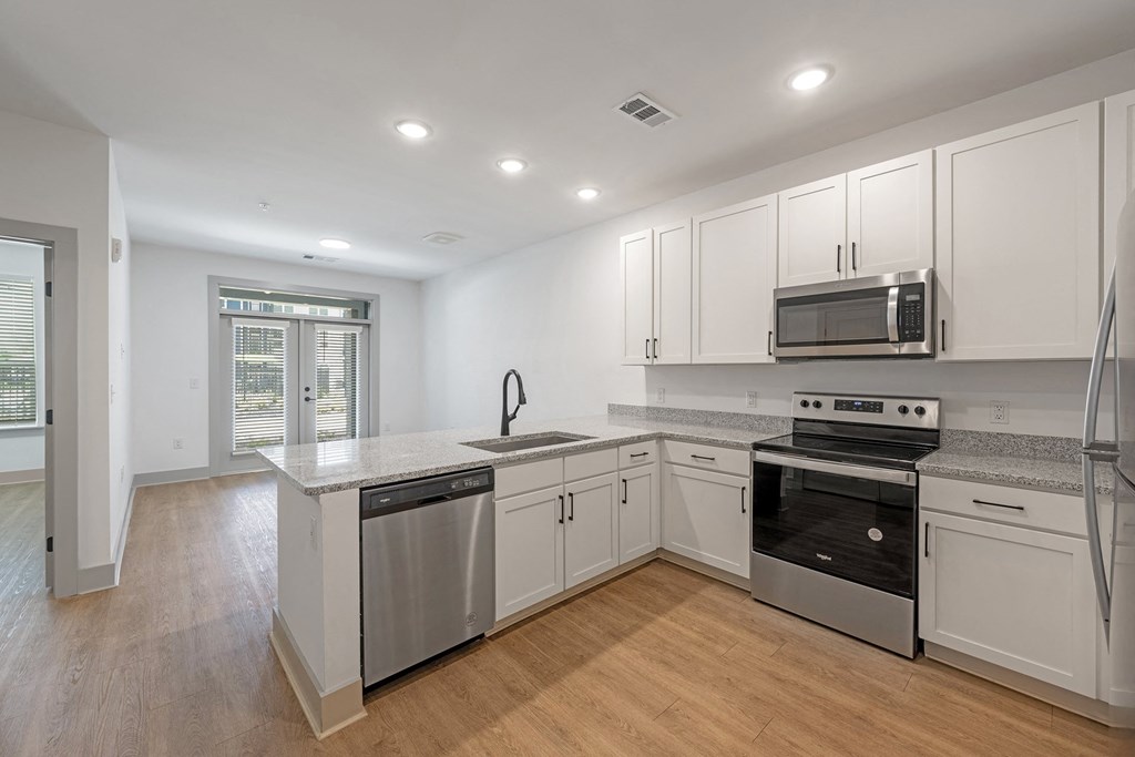 3 BR Luxury Apartments in Huntsville AL - The Kelvin - Modern L-Shaped Kitchen with Wood-Style Flooring, Stainless Steel Appliances, Granite Countertops, White Shaker-Style Cabinetry, and Overhead Lights