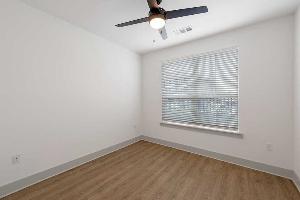 One BR Luxury Apartments in Huntsville AL - The Kelvin - Unfurnished Bedroom Area with Wood-Style Flooring, White Walls, Ceiling Fan, and Window with Blinds