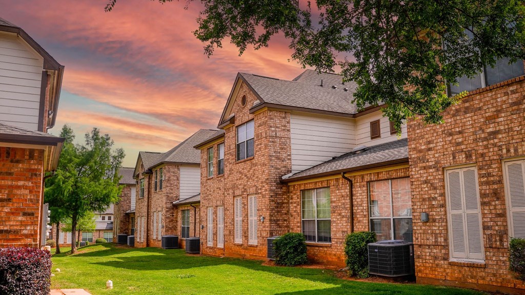 a row of brick houses with green grass and a cloudy sky