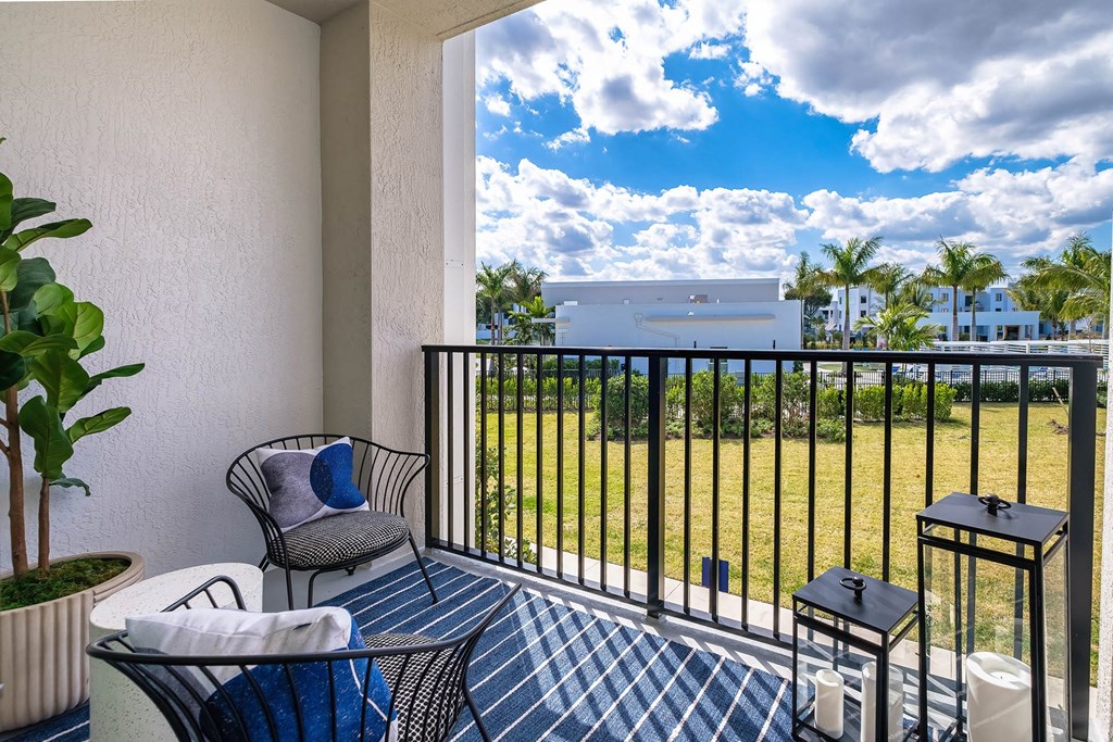 a balcony with chairs and a table and a view of a field and a house at Altis Blue Lake, Florida, 33467