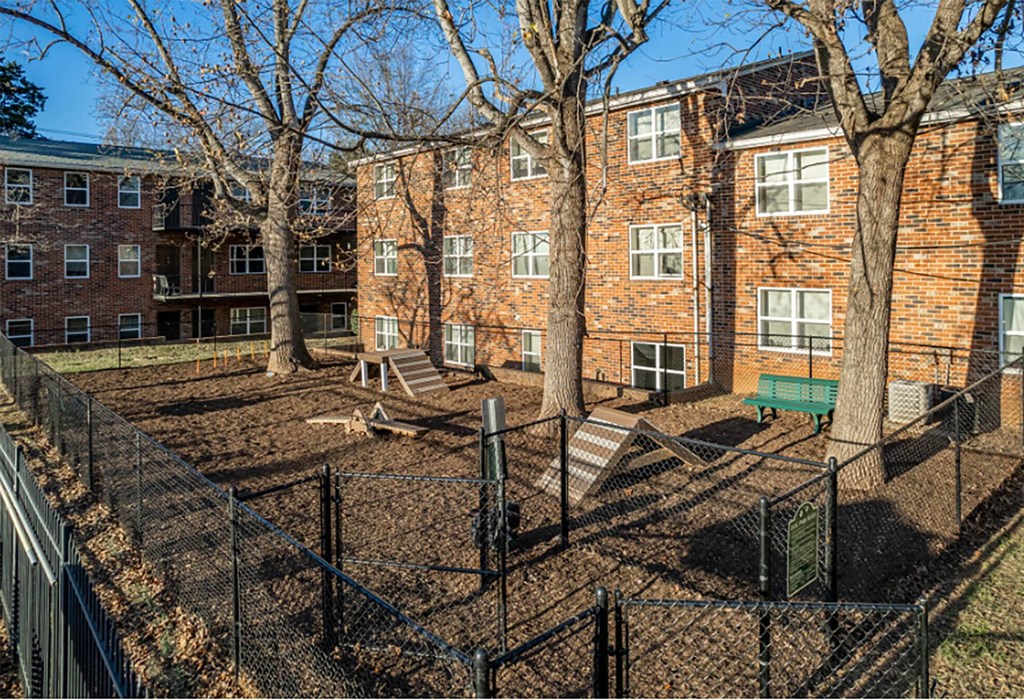 a fenced in area with a bench and trees in front of a brick building