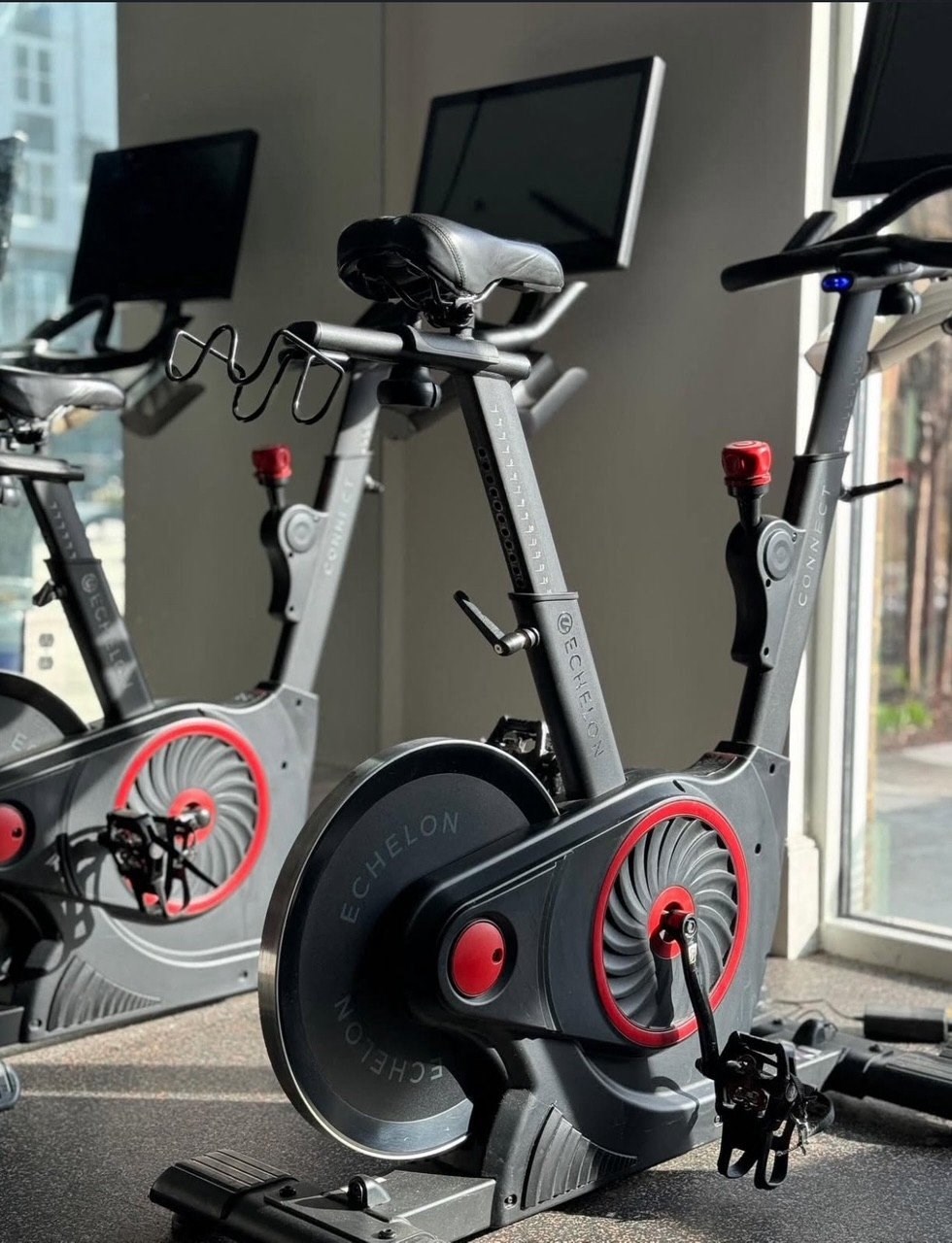 A stationary exercise bike with a red flywheel is in a room with a window.