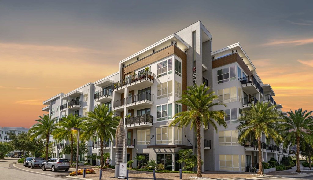 A modern apartment building with balconies and palm trees in front.