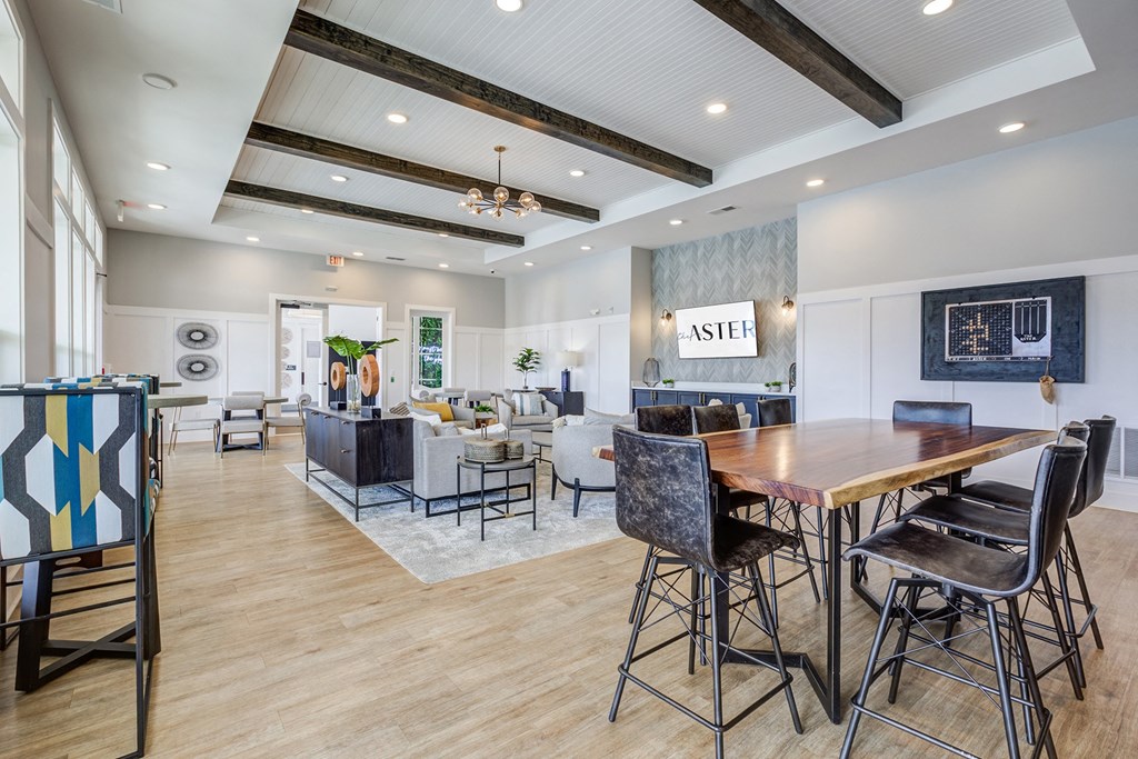 Downtown Greenville, SC Apartments - The Aster - Resident Clubroom with High Ceilings, Vinyl Plank Flooring, Area Rug, Mounted Television, Seating Area, Table, and Chairs.