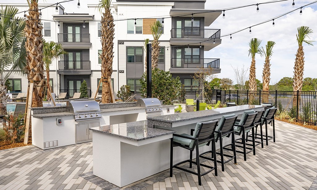 an outdoor kitchen with a bar and chairs in front of an apartment building in apollo beach, florida