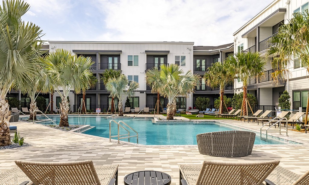 a swimming pool with chairs and palm trees in front of a building in apollo beach, florida