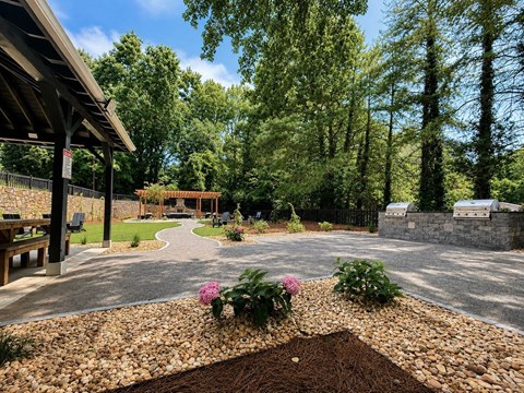 A garden with a gravel path and a bench under a wooden structure.