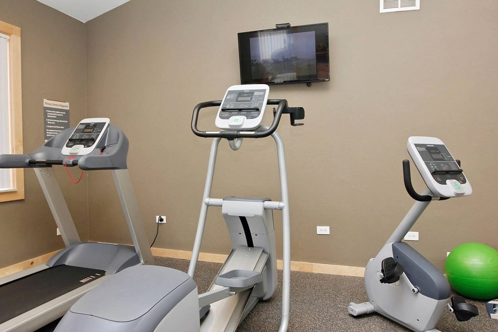 A gym with treadmills, exercise bike and a television mounted on the wall.