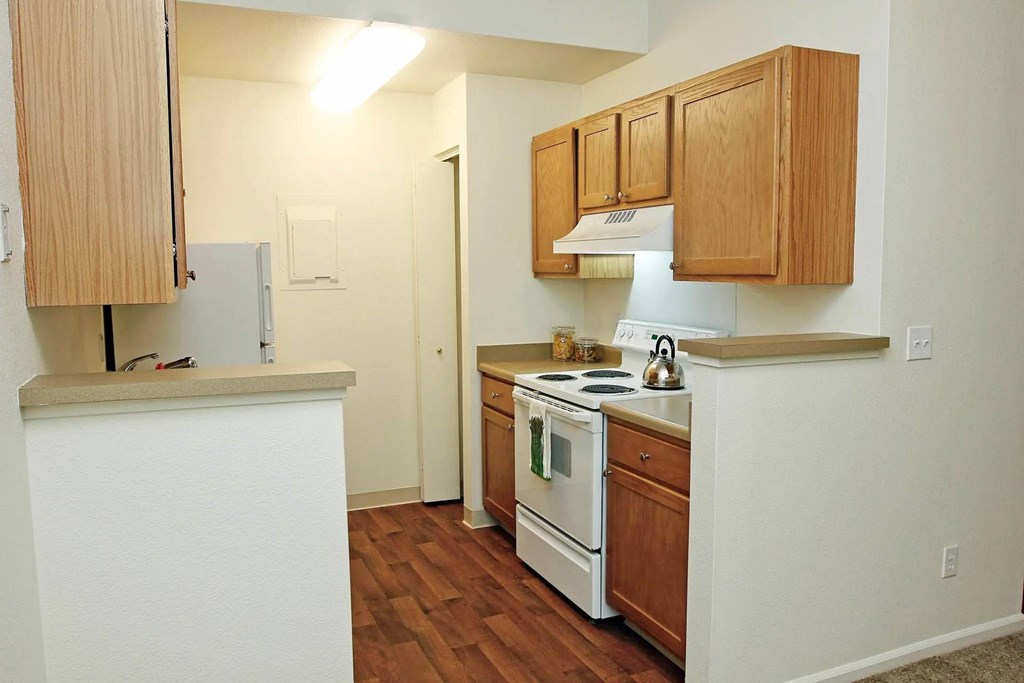 A kitchen with a white stove top oven and wooden cabinets.