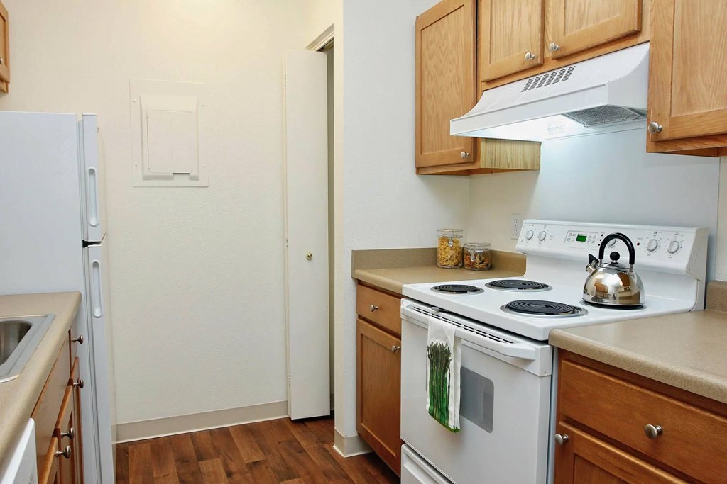 A white stove with a kettle on it is in a kitchen with wooden cabinets.