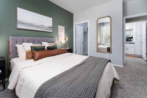 Alexandria, KY, Apartments with In-Unit Washer and Dryer - Elevation Apartment Homes - Bedroom with 9-Foot Ceiling, Carpet Flooring, Large Bed with Pillows, Nightstands, Lamp, Wall Arts, Wall Mirror, and a View of the Oversized Closet and Bathroom.