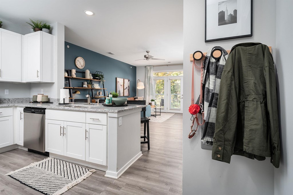 A kitchen with white cabinets and a green jacket hanging on the wall.