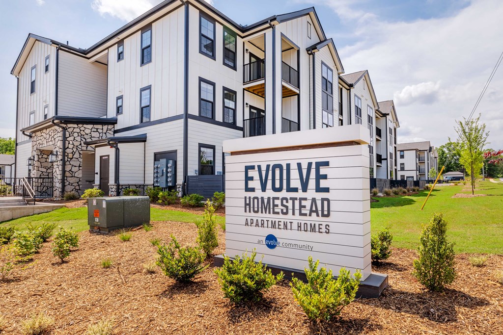 A sign for Evolve Homestead Apartment Homes stands in front of a building.