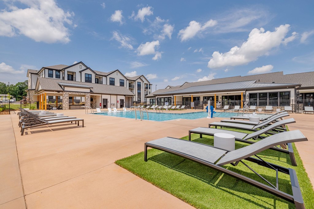 A large outdoor swimming pool with sun loungers and a building in the background.