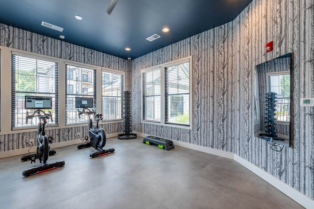A room with a wallpapered wall and a row of stationary bikes.
