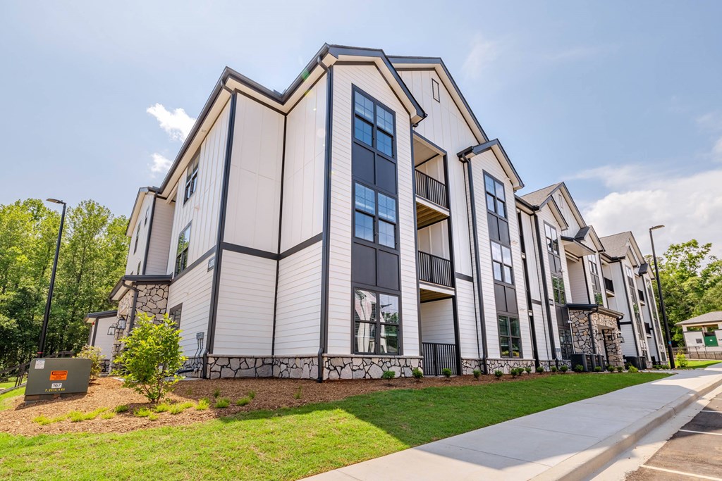 A modern building with a white facade and dark trim is surrounded by a grassy area and a sidewalk.