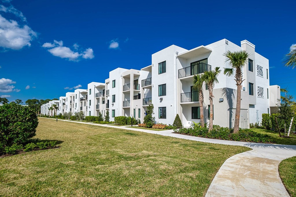 a row of white apartment buildings with palm trees in front of them at Altis Blue Lake, Lake Worth, FL