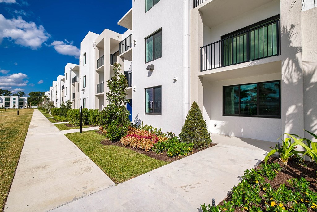 a sidewalk in front of a building with grass and plants at Altis Blue Lake, Lake Worth, 33467