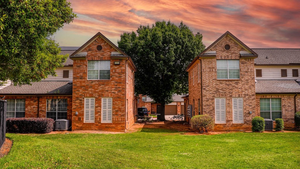 a red brick house with a green lawn and a cloudy sky