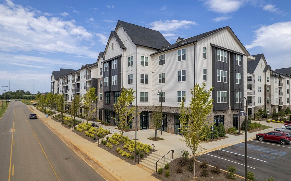 Dog-Friendly Apartments in Madison, Alabama - The Dempsey - Street View of Apartment Complex Showing Sidewalk, Lamp Posts, Plants, Trees, and Parking Lot.