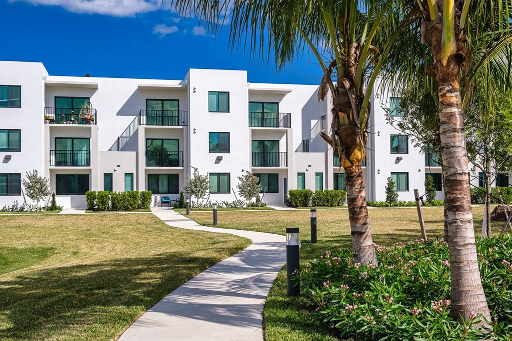 an apartment building with a sidewalk and palm trees at Altis Blue Lake, Lake Worth, Florida