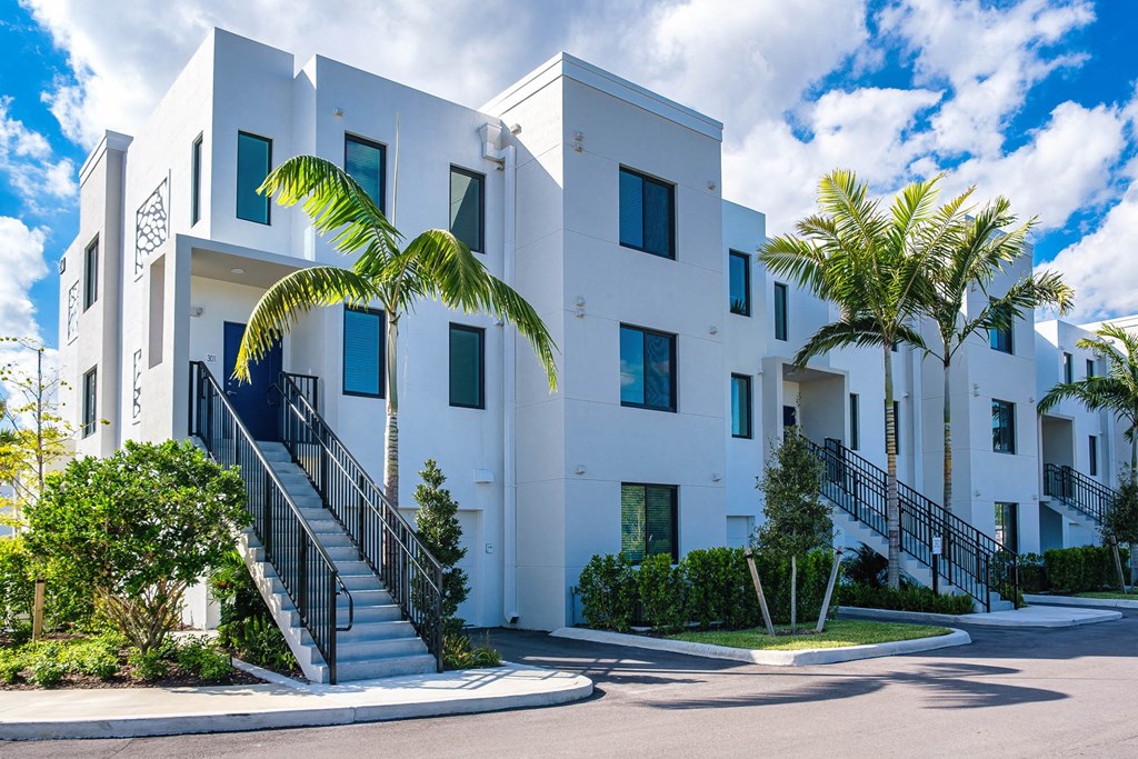 a building with stairs and palm trees in front of it at Altis Blue Lake, Lake Worth, 33467