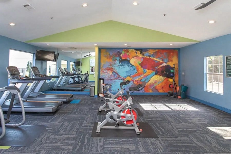 a gym with cardio machines and a colorful mural on the wall