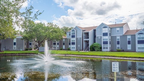 a fountain in the pond with an apartment building in the background