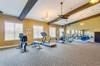 a gym with cardio machines and windows and a ceiling fan