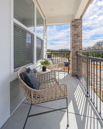 a balcony with two wicker chairs and a table and a window