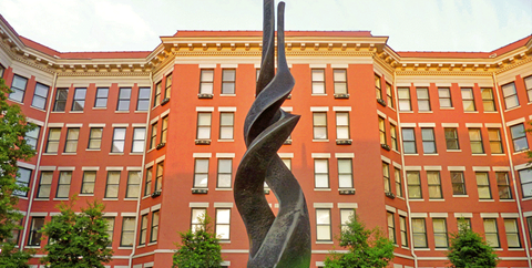 A large building with a red brick facade and a sculpture in front.