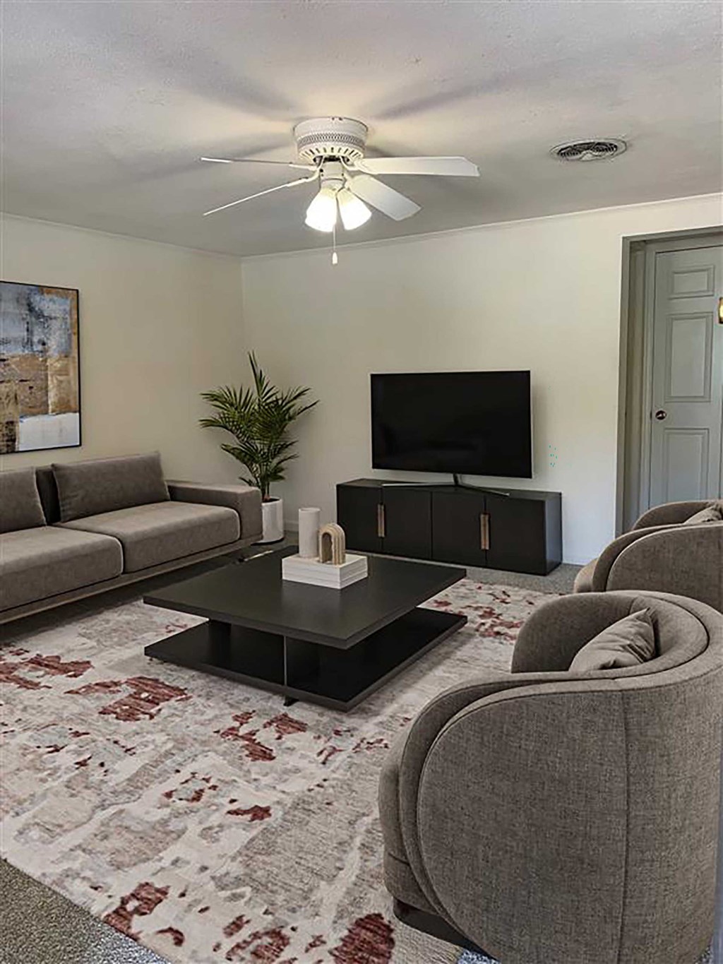 A living room with a grey sofa, a black coffee table, a flat screen TV and a ceiling fan.