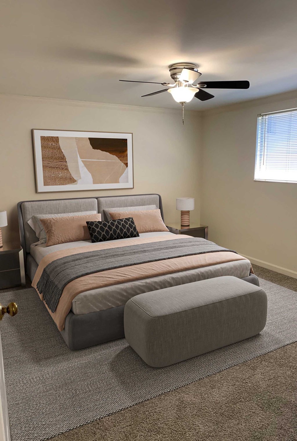 A bedroom with a bed, pillows, a ceiling fan, and a painting on the wall.